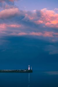 Lighthouse by sea against sky during sunset