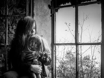 Young adult sitting and holding a doll on an abandoned room near a window.