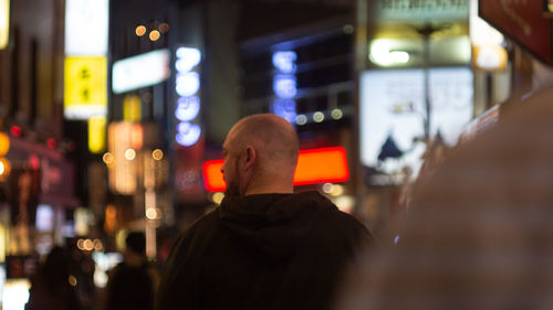 Rear view of man standing against illuminated city at night