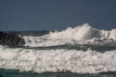 Waves splashing on shore against clear sky