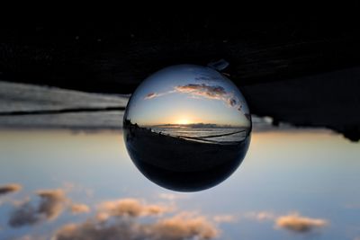 Close-up of crystal ball on water against sky