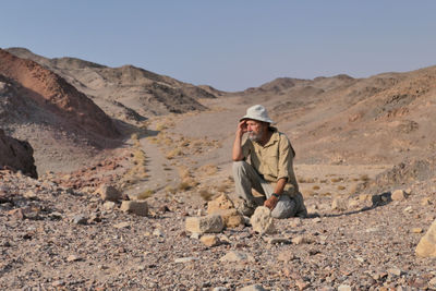 Senior man on rock in desert against sky