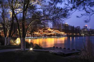 Illuminated trees by lake against sky at dusk