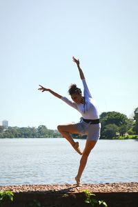 Full length of woman dancing by river against clear sky