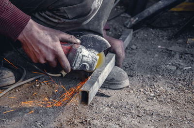 Low section of worker using power tool on metal at workshop