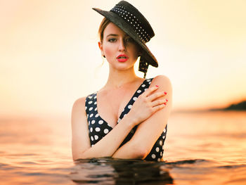 Young woman wearing hat against sea during sunset