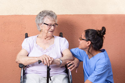 Happy senior woman with walking stick in wheelchair with her caregiver at home.