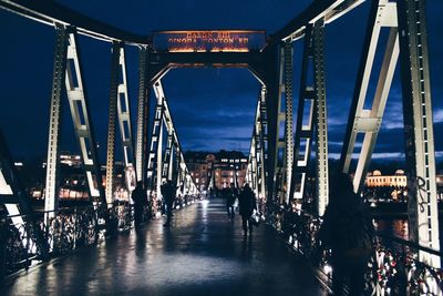 People on metallic footbridge against sky at night