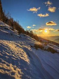 Snow covered land against sky during sunset