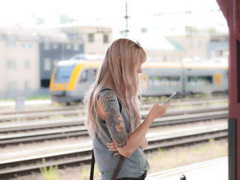 Woman using phone while standing on railroad station