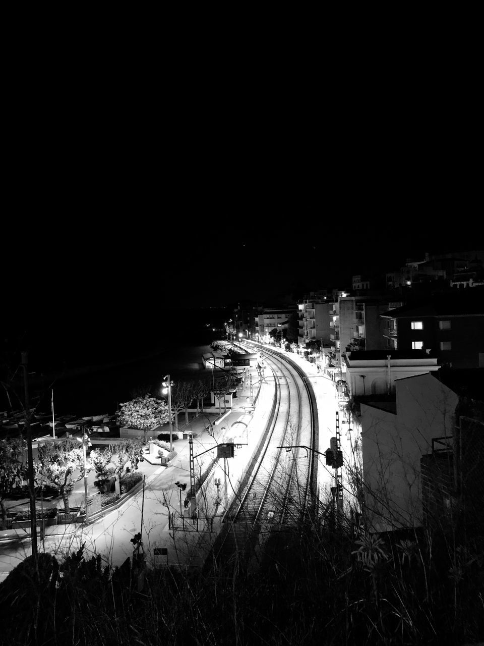 HIGH ANGLE VIEW OF ILLUMINATED ROAD BY BUILDINGS IN CITY AT NIGHT