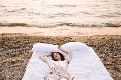 Young woman wearing stylish pajamas lying in bed at sea shore outdoors close up. good morning. 
