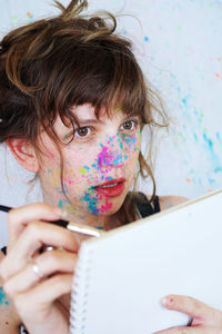 Close-up of woman covered in powder paint holding paintbrush and notebook