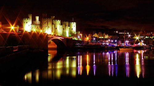 Illuminated city by river against sky at night