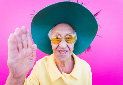 Portrait of senior woman showing stop gesture against pink background