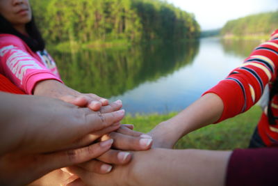 Close-up of people stacking hands by lake
