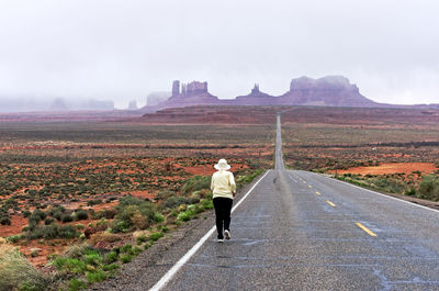 Rear view of woman running on country road against sky