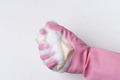 Close-up of hand holding pink cake against white background