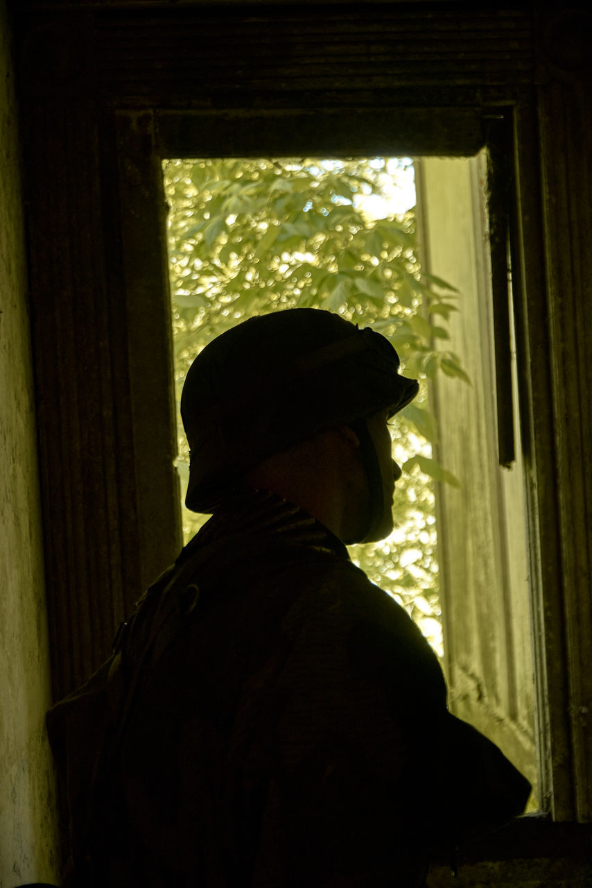 REAR VIEW OF MAN LOOKING THROUGH WINDOW IN BUILDING
