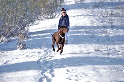 Full length of teenage boy standing by dog on snowy land