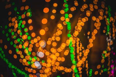 Defocused illuminated lights hanging on tree at night