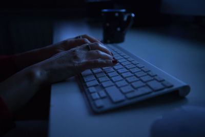 Cropped hands of woman using computer keyboard on table in darkroom at home