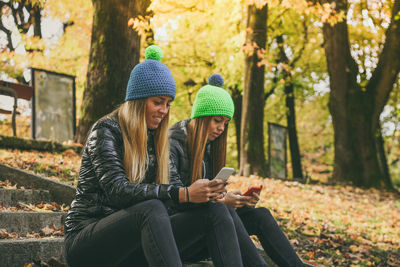 Two girls sitting in the park using smartphone. teen using mobile phone. sisters chat with friends.