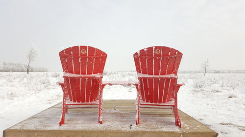 Red deck chairs on snow against water