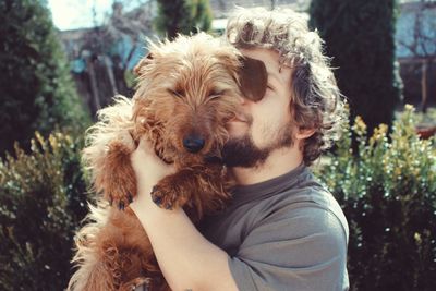 Close-up of smiling young man pampering dog at park during sunny day