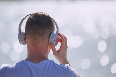 Rear view of man listening music against lens flare