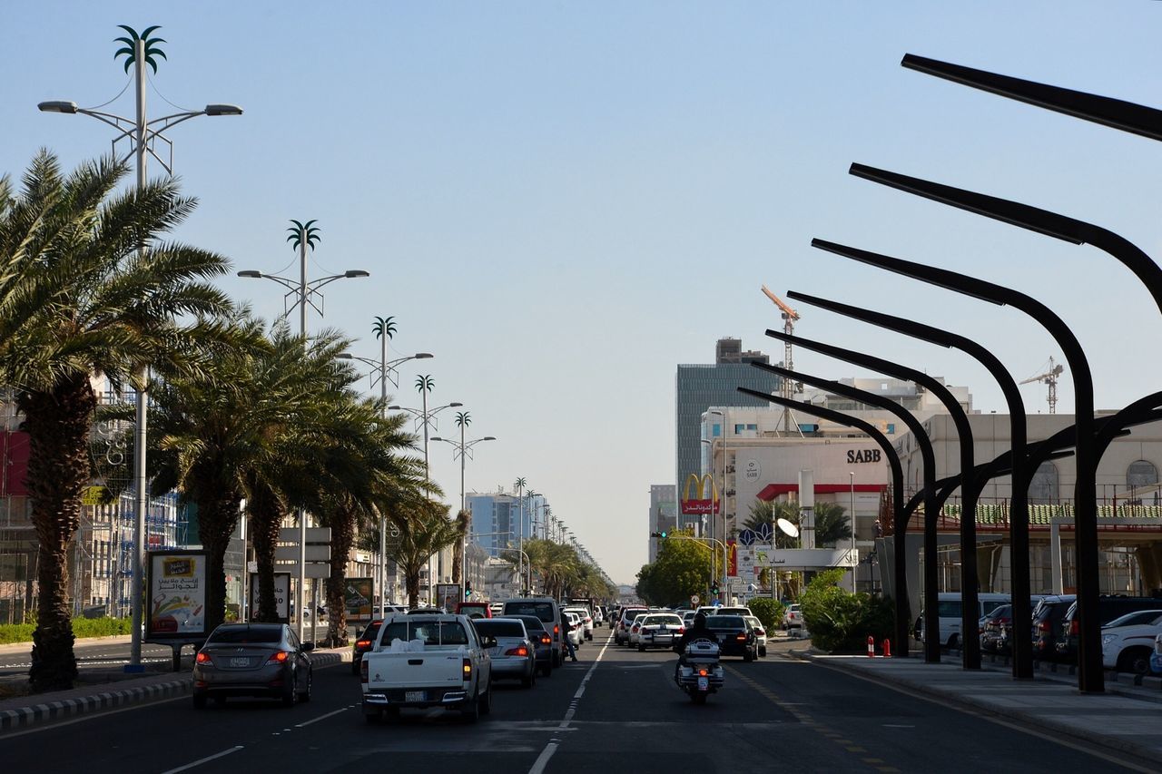 transportation, car, land vehicle, building exterior, city, architecture, mode of transport, built structure, street, clear sky, road, traffic, city life, city street, tree, road marking, on the move, street light, skyscraper, incidental people