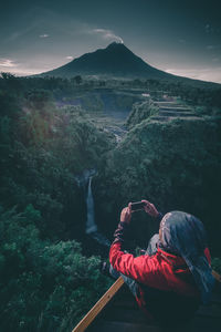 Man photographing with mobile phone against mountains