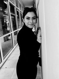 Portrait of smiling young woman standing against door