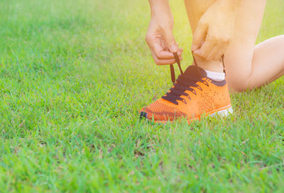 Low section of woman tying shoelace on grassy field at park