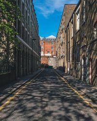 Shadow of trees on road amidst buildings on sunny day