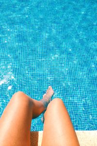 Low section of young woman relaxing at poolside on sunny day