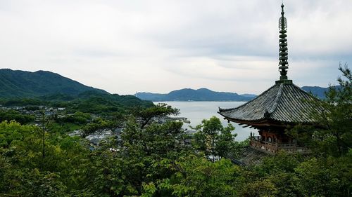 Scenic view of building by trees and mountains against sky