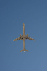 Low angle view of airplane flying against clear blue sky