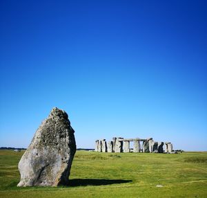 Ancient structure of stonehenge on field against clear blue sky