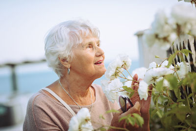 Elderly woman admiring beautiful bushes with white roses