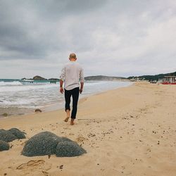 Rear view of woman standing on beach against sky