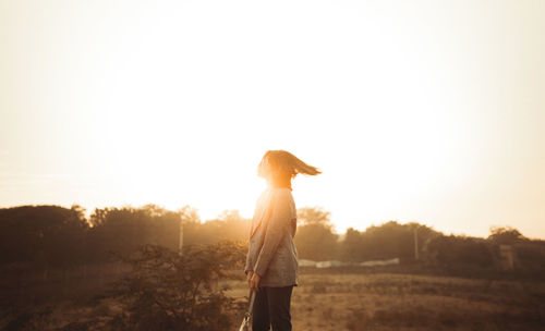 Rear view of woman standing against sky during sunset