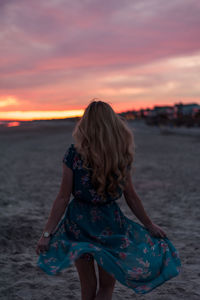 Young woman at beach against sky during sunset