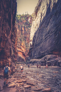 People on rock formation by mountain against sky