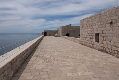 View of footpath by sea against cloudy sky