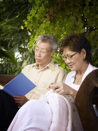 Senior man reading book while woman knitting sweater in backyard