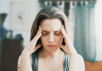 Close-up of young woman with eyes closed touching forehead