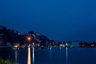 Illuminated cityscape by sea against clear blue sky at night