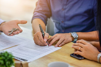 Cropped hand of real estate agent holding key by customer signing contract on table