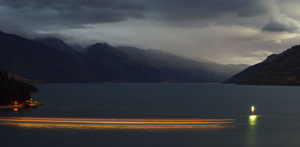 Light trails on road by lake against sky at night